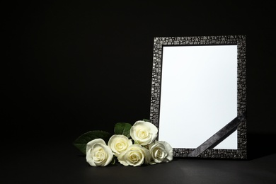 Photo of Funeral photo frame with ribbon and white roses on dark table against black background. Space for design