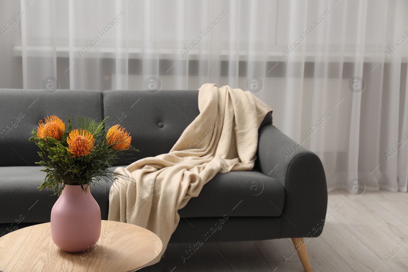 Photo of Vase with beautiful flowers on wooden coffee table near grey sofa in room