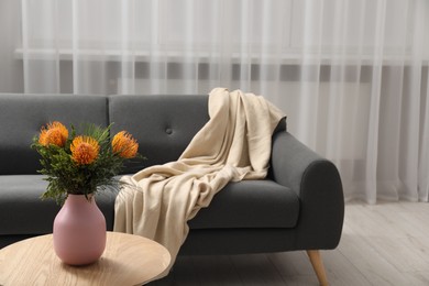 Vase with beautiful flowers on wooden coffee table near grey sofa in room