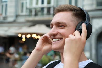 Photo of Smiling man in headphones listening to music outdoors. Space for text