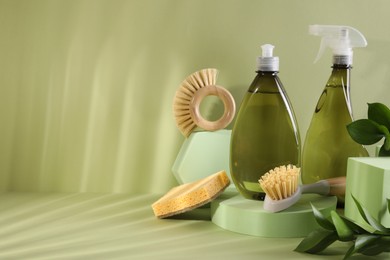 Bottles of cleaning product, sponge and brushes on light green background. Space for text