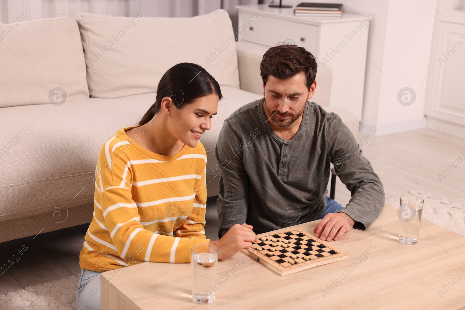 Photo of Happy couple playing checkers at coffee table in room