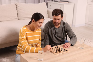 Happy couple playing checkers at coffee table in room