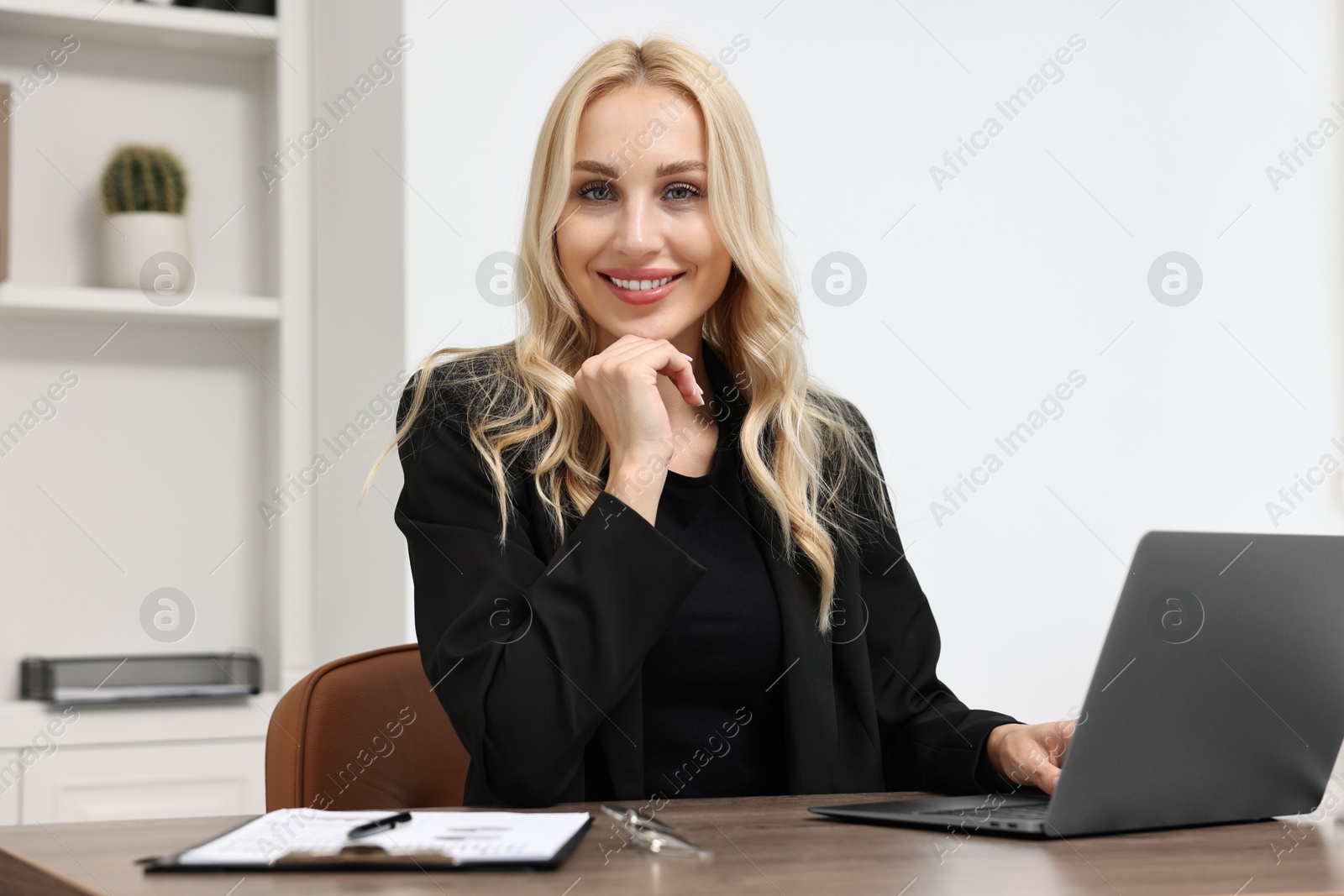 Photo of Happy secretary at table with laptop and stationery in office