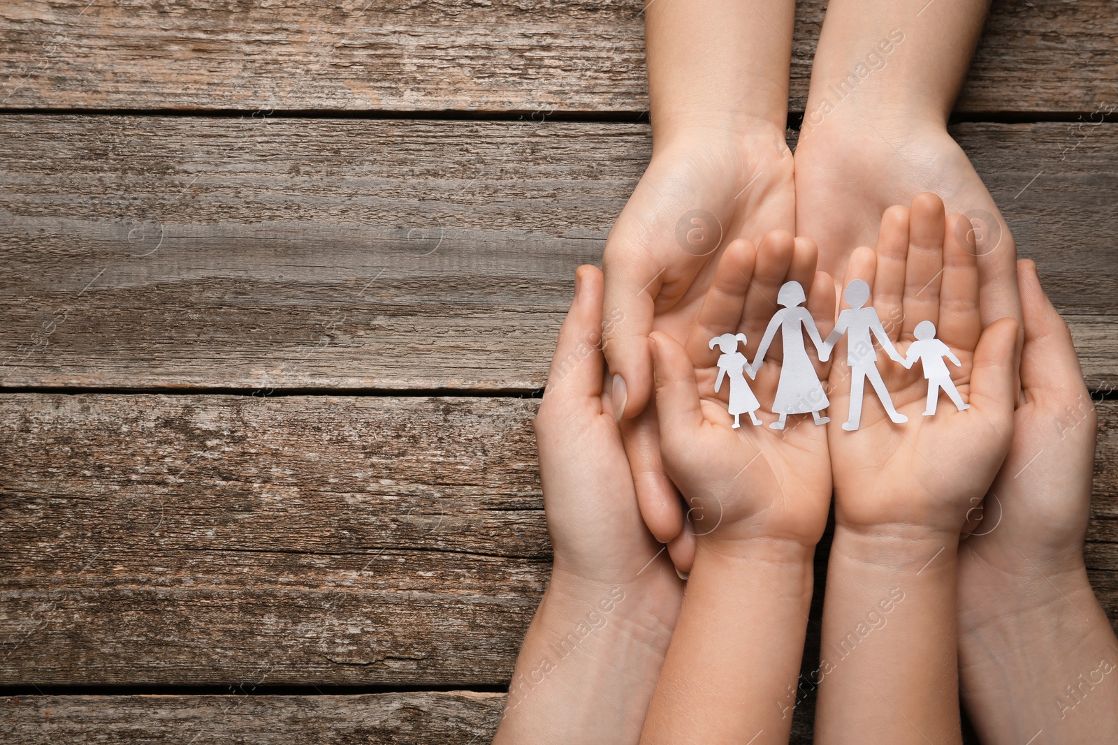 Photo of Parents and child holding paper cutout of family at wooden table, top view. Space for text