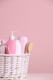 Wicker basket with baby cosmetic products and bath accessories on white table against pink background. Space for text