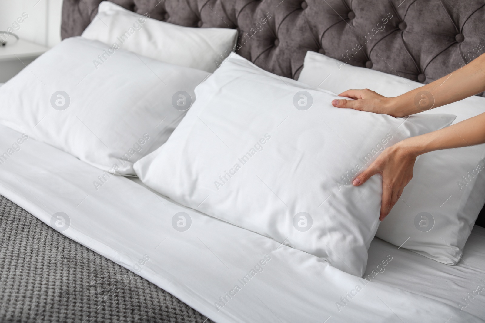 Photo of Young woman plumping white pillow on bed, closeup