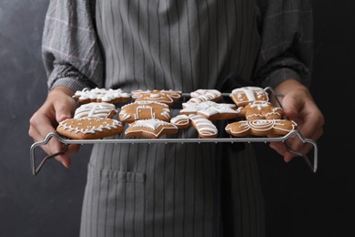 Photo of Woman holding cooling rack with delicious homemade Christmas cookies on black background, closeup