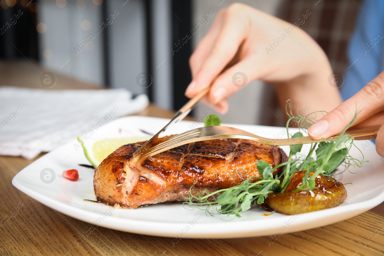 Photo of Woman eating delicious grilled duck breast served at wooden table, closeup