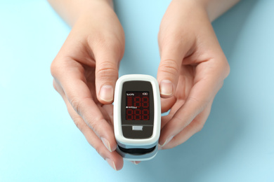 Woman holding fingertip pulse oximeter on light blue background, closeup