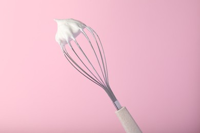 Whisk with whipped egg whites on pink background