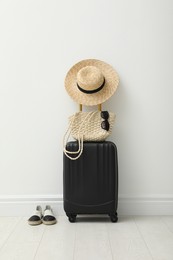 Photo of Suitcase packed for trip, shoes and summer accessories near white wall indoors