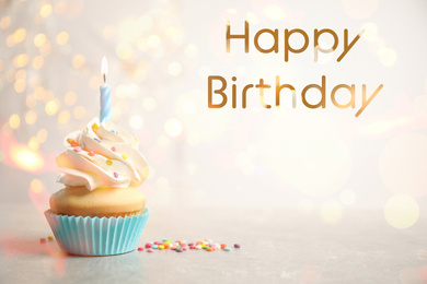 Image of Delicious cupcake with candle on light table against blurred lights. Happy Birthday