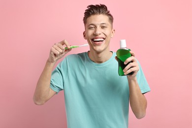 Young man with mouthwash and toothbrush on pink background