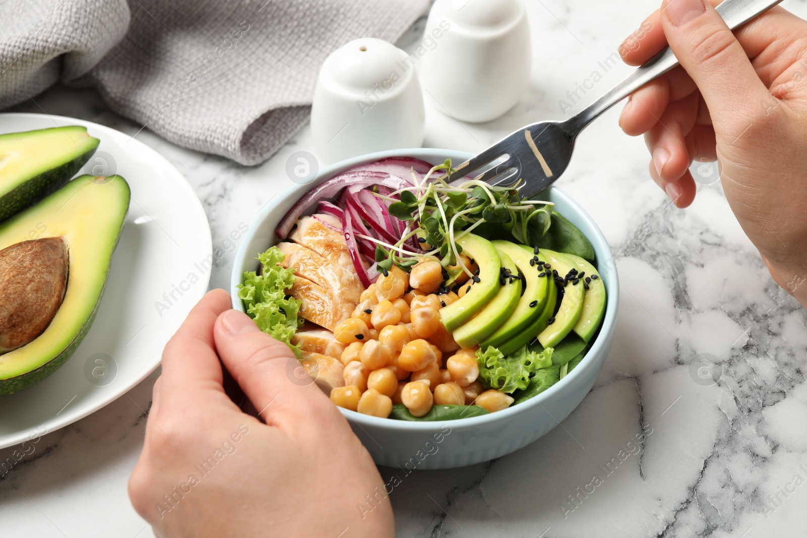 Photo of Woman eating delicious avocado salad with chickpea at white marble table, closeup