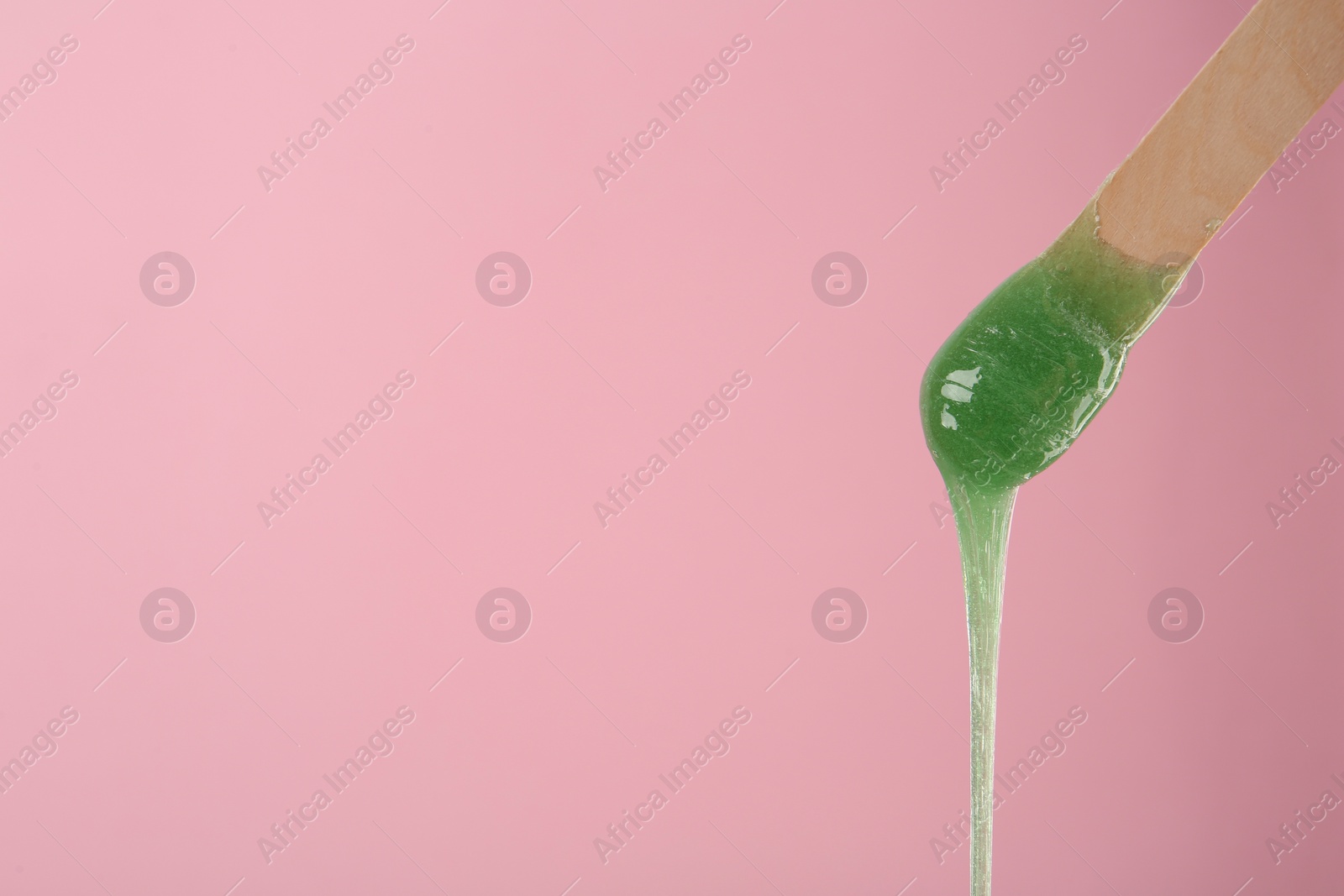 Photo of Wooden spatula with hot depilatory wax on pink background. Space for text