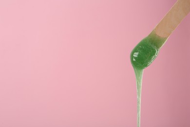 Wooden spatula with hot depilatory wax on pink background. Space for text