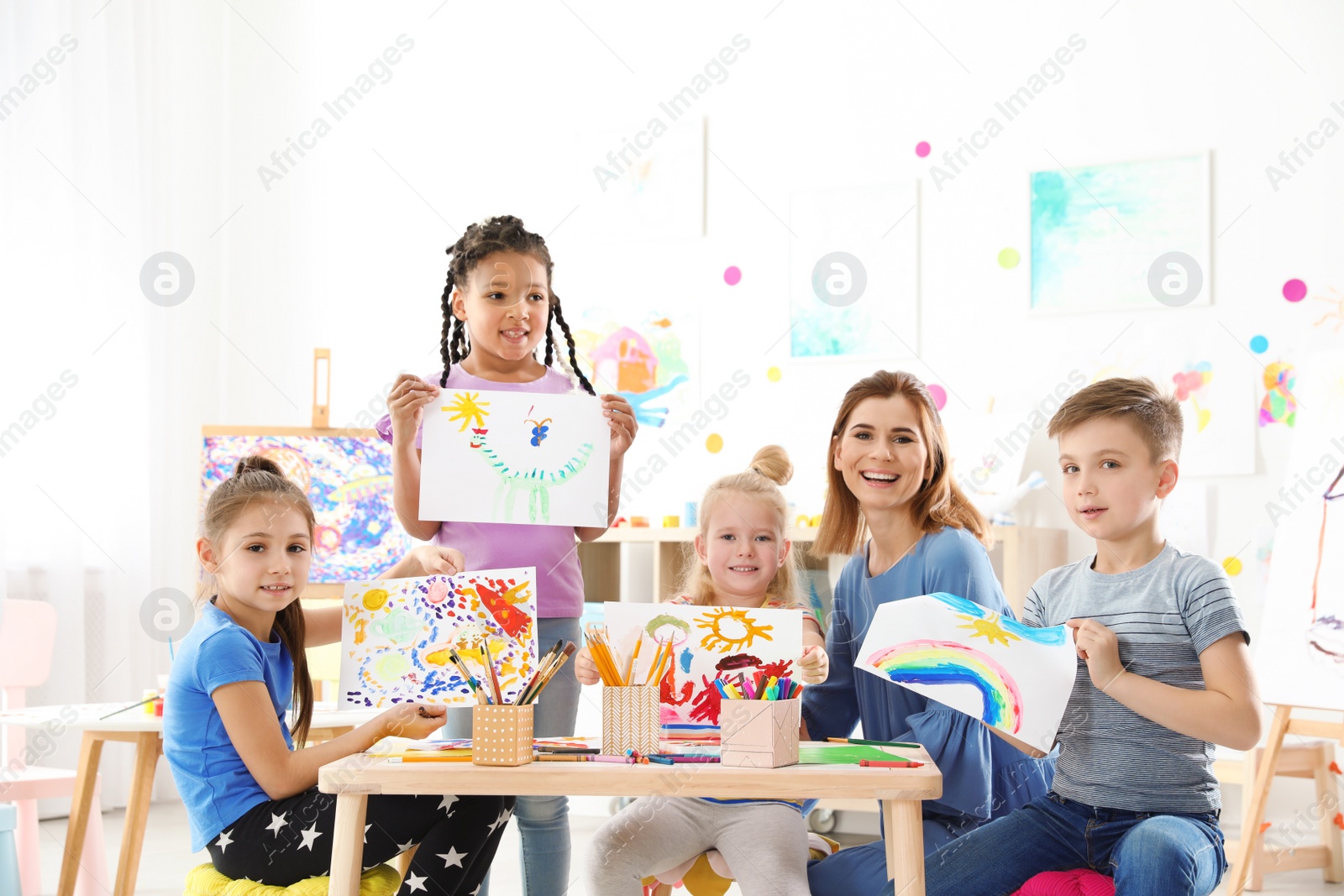 Photo of Cute little children with teacher showing their paintings at lesson indoors