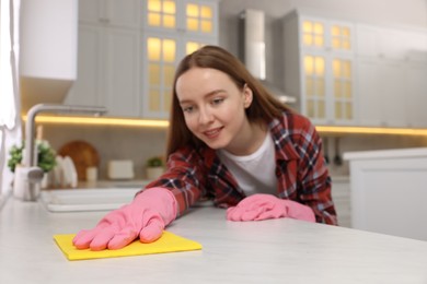 Photo of Woman cleaning white marble table with microfiber cloth in kitchen, selective focus