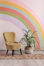Comfortable chair, runner rug and houseplant near white wall with rainbow art indoors