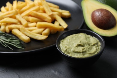 Photo of Plate with french fries, guacamole dip and avocado served on black table, closeup