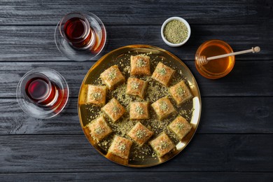 Photo of Delicious fresh baklava with chopped nuts served on black wooden table, flat lay. Eastern sweets