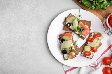 Photo of Tasty rye crispbreads with salmon, cream cheese and vegetables served on light grey table, flat lay. Space for text