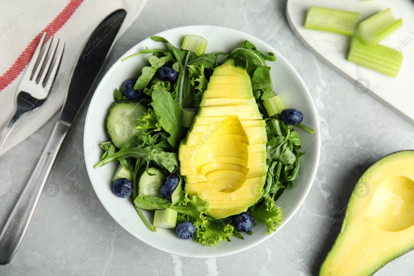 Photo of Delicious avocado salad with blueberries in bowl on grey marble table, flat lay