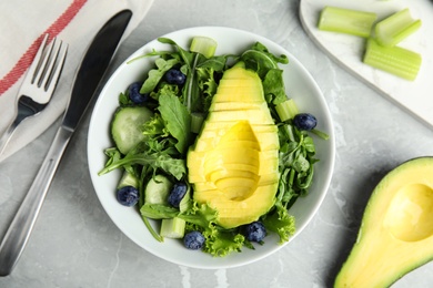 Photo of Delicious avocado salad with blueberries in bowl on grey marble table, flat lay