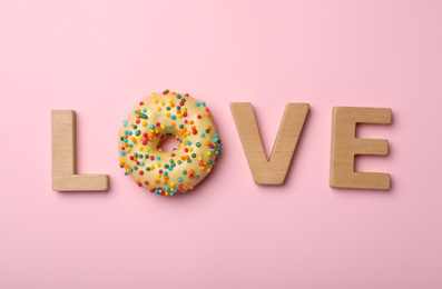 Photo of Word LOVE made with wooden letters and donut on pink background, flat lay