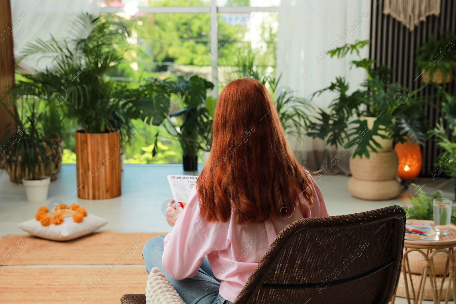 Photo of Woman reading magazine in armchair at indoor terrace, back view