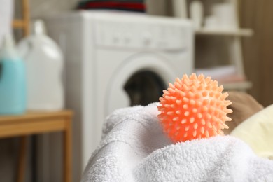Photo of Orange dryer ball and towels near washing machine in laundry room, closeup. Space for text