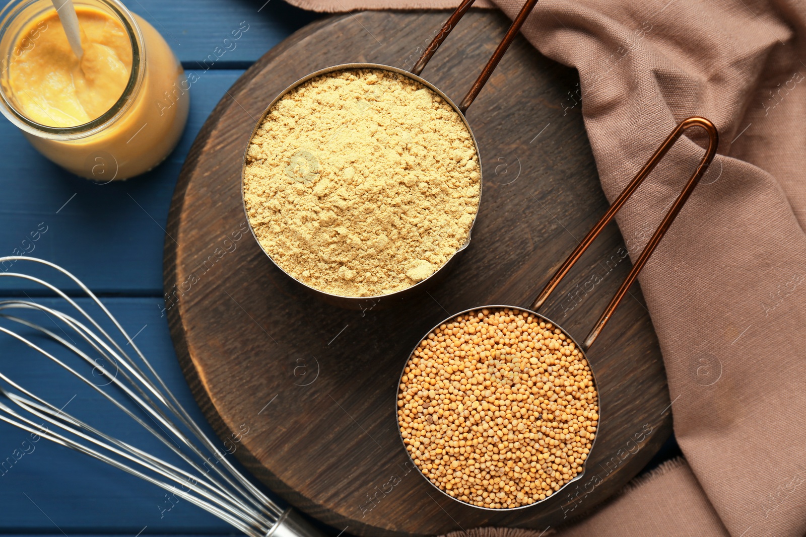 Photo of Saucepans with mustard powder and seeds on blue wooden table, flat lay