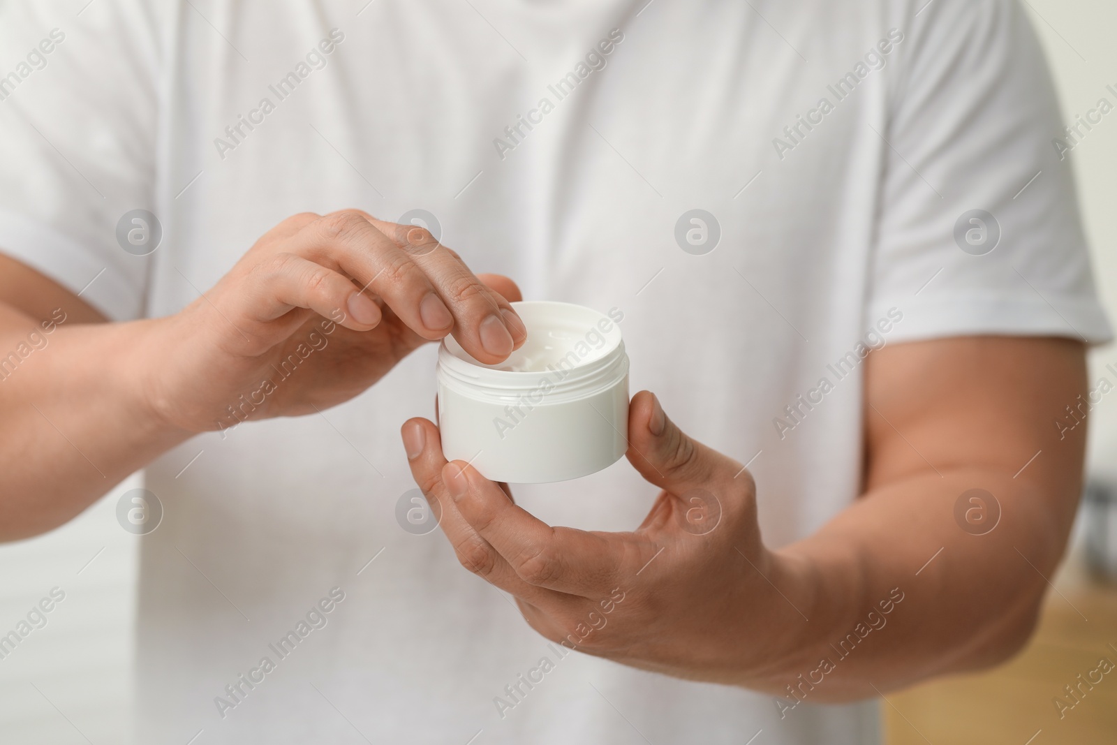 Photo of Man with jar of body cream indoors, closeup