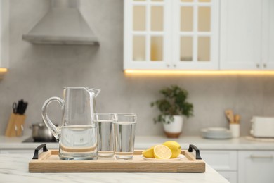 Jug, glasses with clear water and lemons on white table in kitchen, space for text