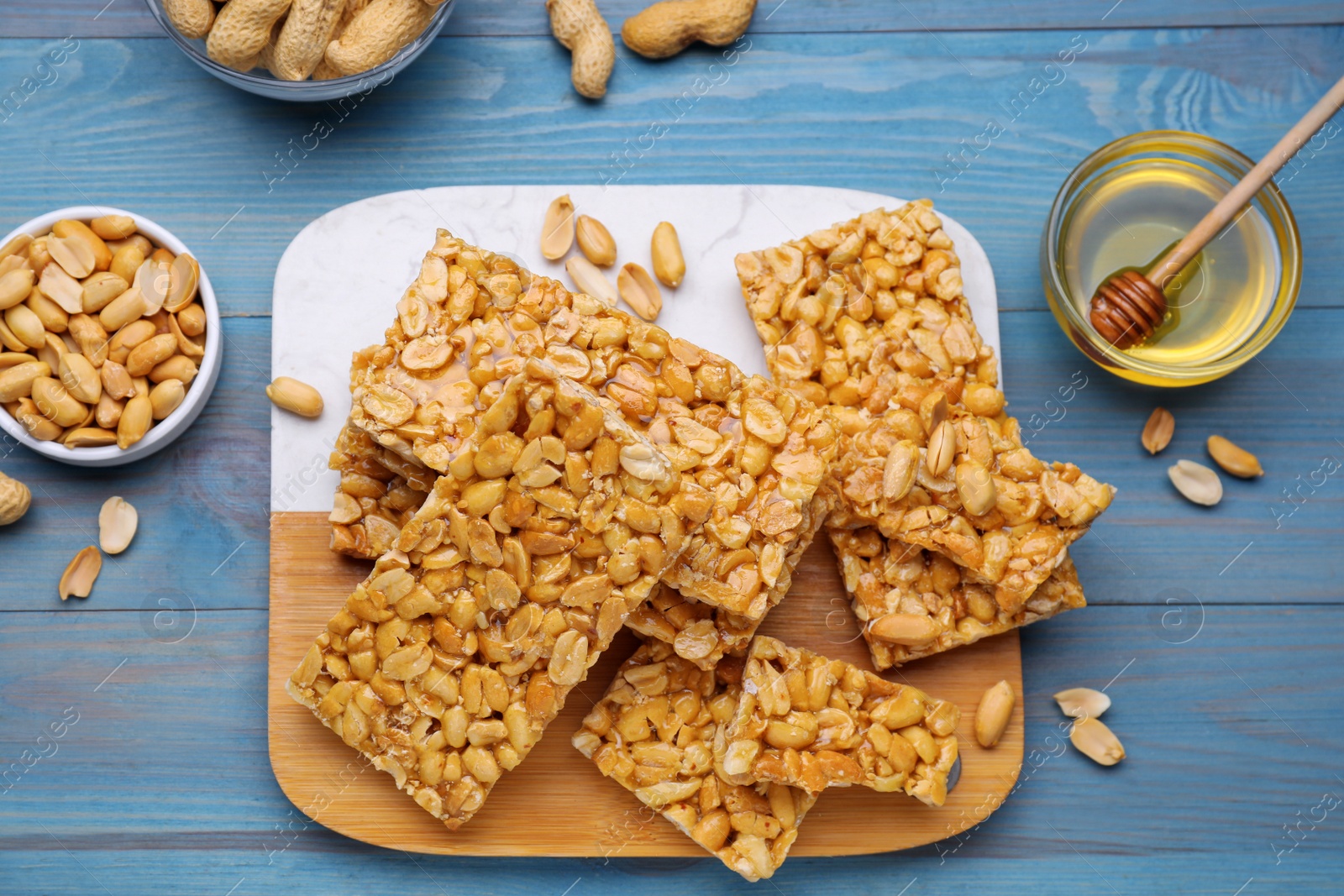 Photo of Delicious peanut bars (kozinaki) and ingredients on light blue wooden table, flat lay