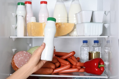 Photo of Woman taking bottle of yogurt from refrigerator, closeup