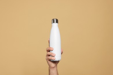 Man holding thermo bottle on beige background, closeup