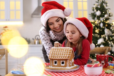 Photo of Mother and daughter decorating gingerbread house at table indoors