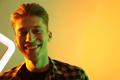 Young man with square lamp on color background in neon lights. Space for text