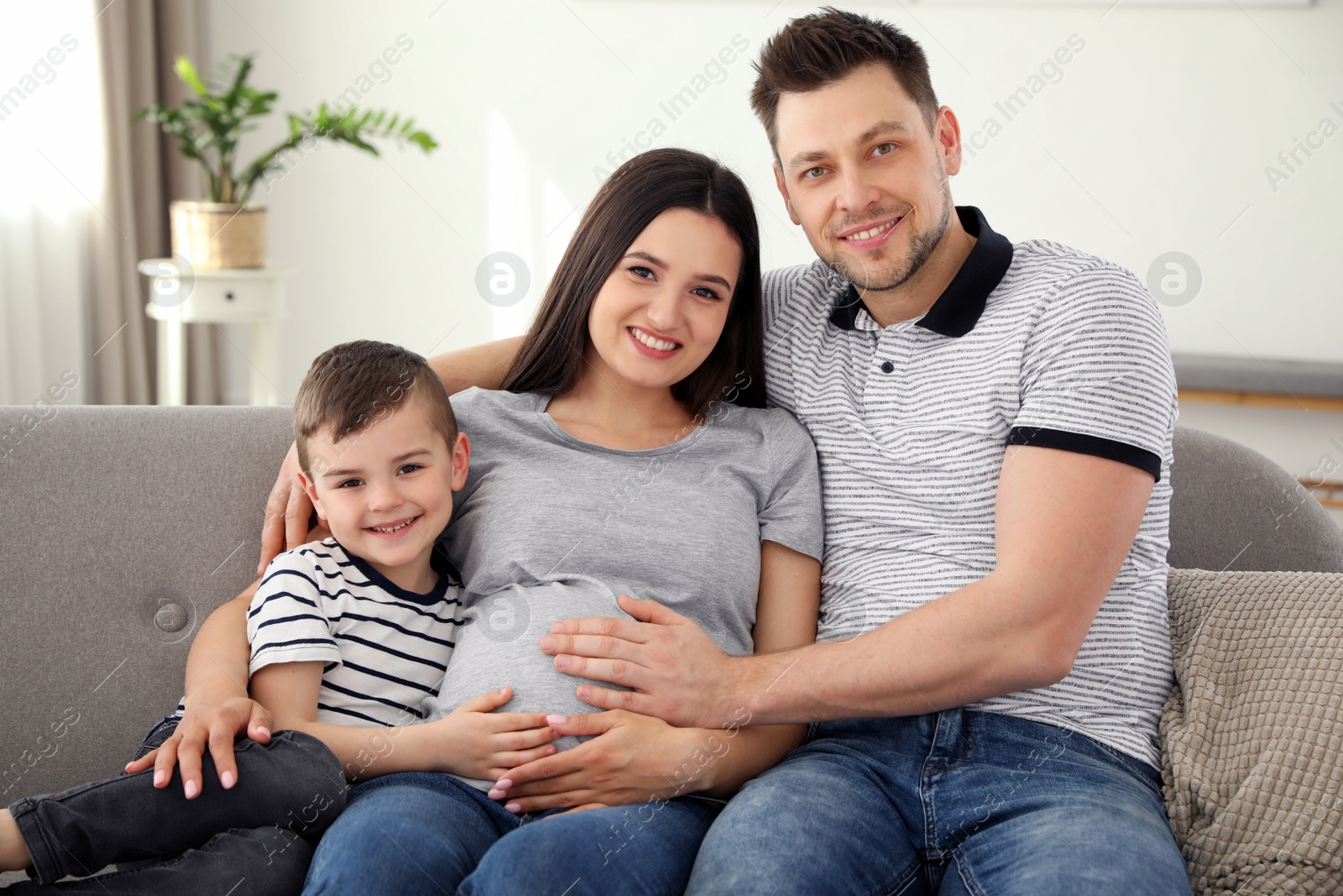 Photo of Father, son and pregnant mother spending time together on sofa at home. Family time