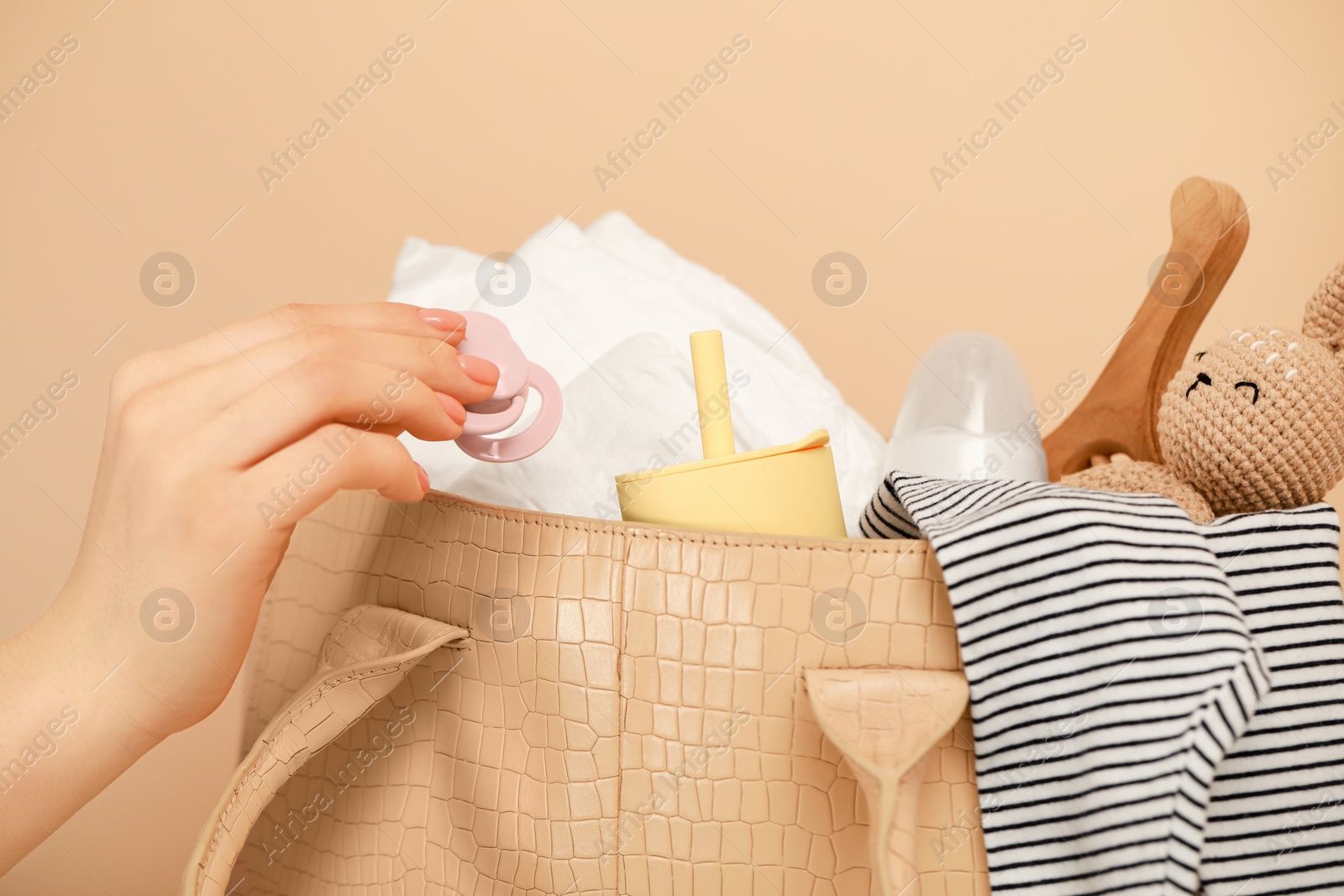 Photo of Woman putting baby`s pacifier into mother`s bag on beige background, closeup