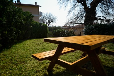 Photo of Empty wooden picnic table with bench in backyard on sunny day