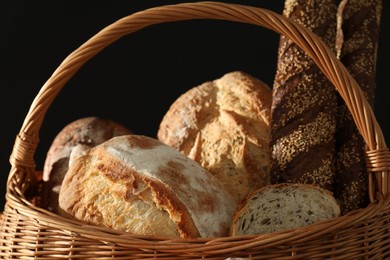 Photo of Wicker basket with different types of fresh bread against black background