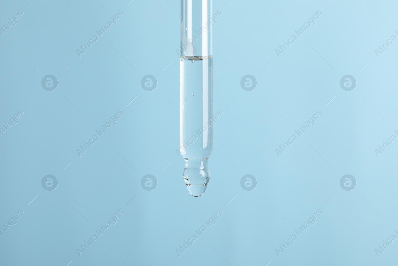 Photo of Dripping cosmetic serum from pipette on light blue background