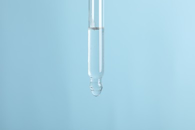 Photo of Dripping cosmetic serum from pipette on light blue background