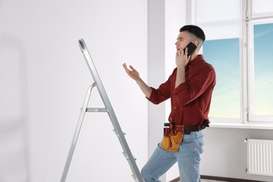 Photo of Handyman talking on phone while climbing up stepladder in room