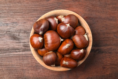 Fresh sweet edible chestnuts on brown wooden table, top view