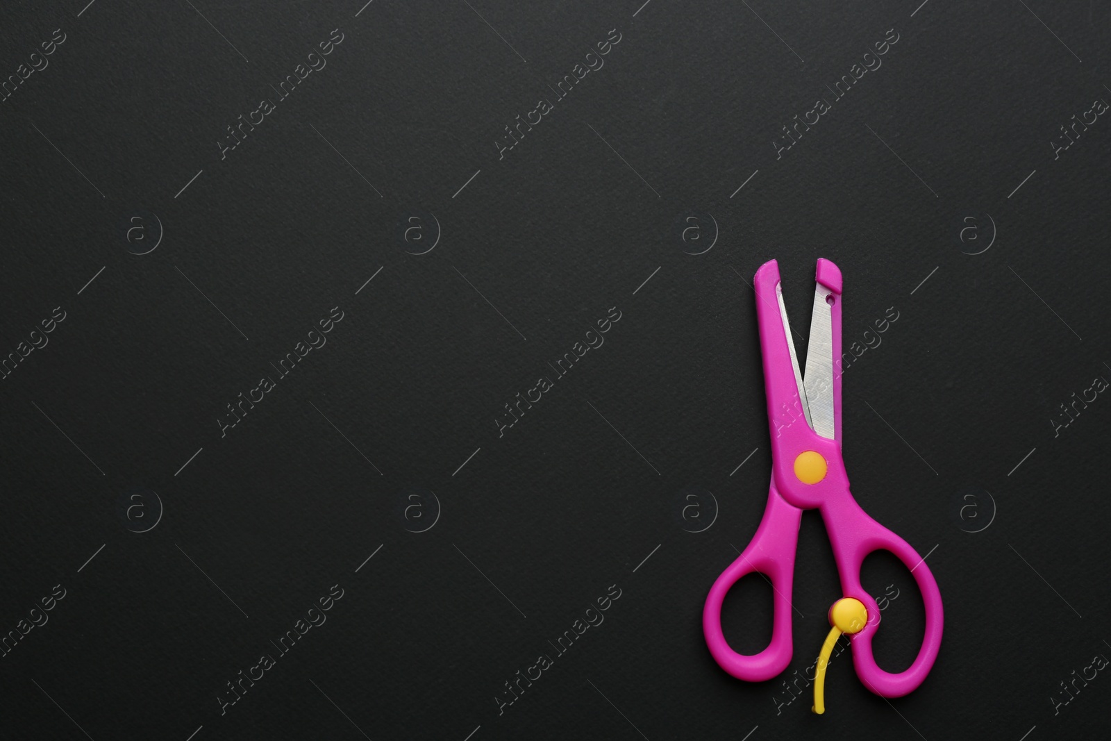 Photo of Pair of training scissors on dark background, top view. Space for text