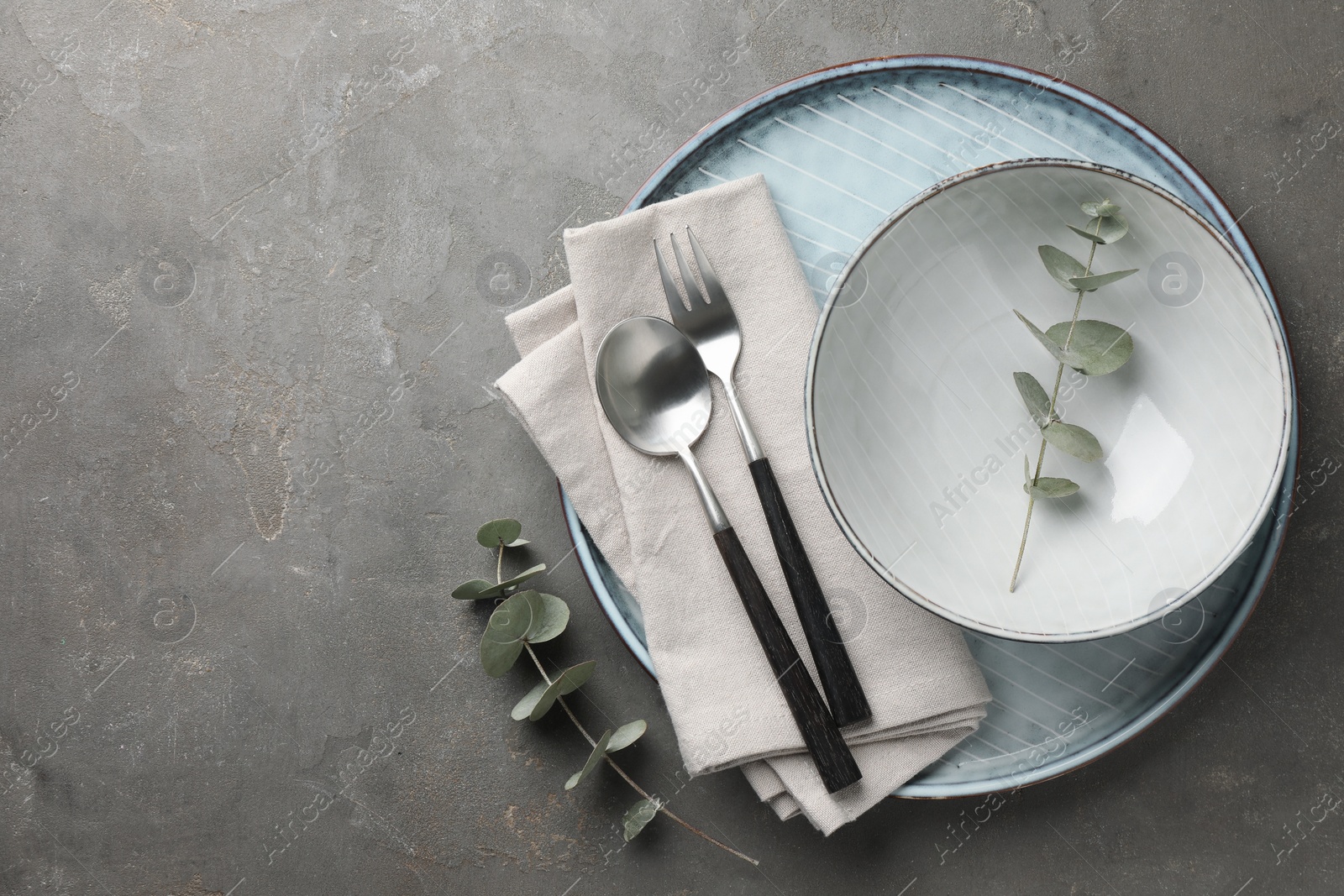 Photo of Stylish setting with cutlery, napkin, eucalyptus branches and plate on grey table, top view. Space for text